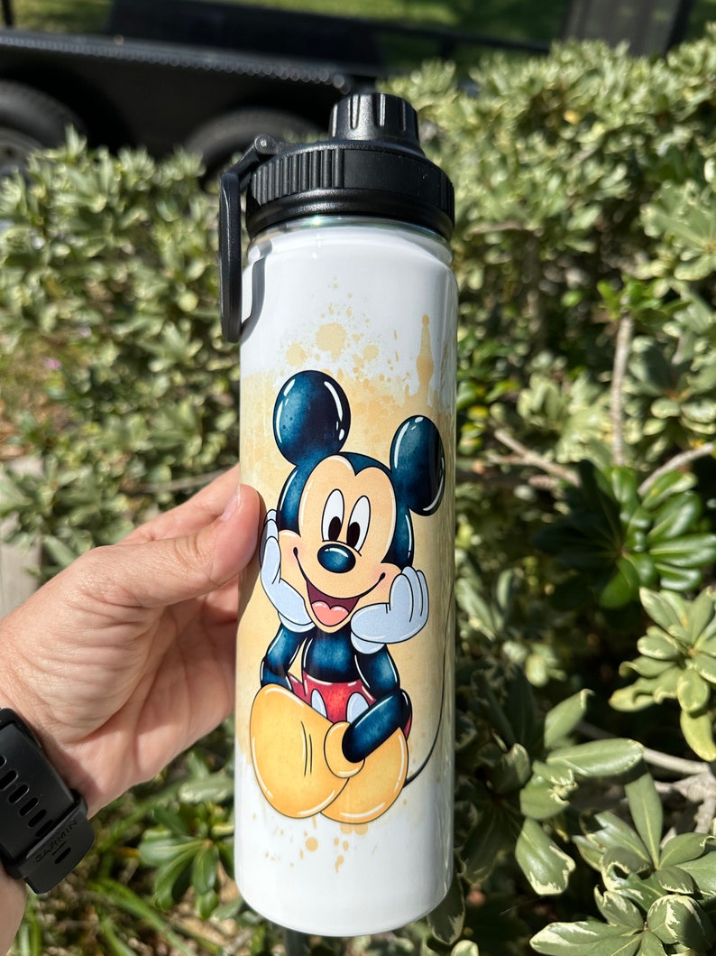 May include: White stainless steel water bottle with a black lid and a cartoon image of Mickey Mouse in a yellow and orange watercolor design.