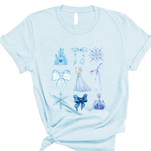 May include: Light blue t-shirt with a variety of blue and white illustrations, including a castle, snowflakes, bows, and a princess figure.