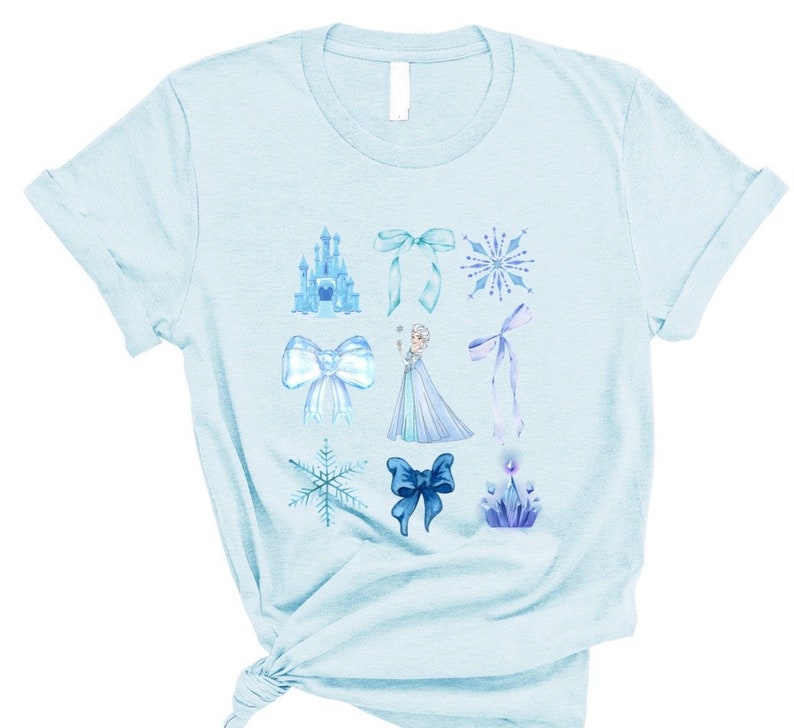 May include: Light blue t-shirt with a variety of blue and white illustrations, including a castle, snowflakes, bows, and a princess figure.