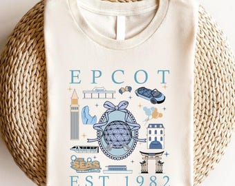 May include: A beige t-shirt with a blue and white illustration of Epcot icons, including the Spaceship Earth, the World Showcase, and the Test Track ride. The text "EPCOT EST 1982" is printed on the shirt.