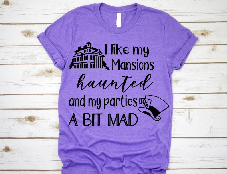 K&ouml;nnte beinhalten: Lilafarbenes T-Shirt mit schwarzem Text, der "Ich mag meine Herrenh&auml;user verflucht und meine Partys ein bisschen verr&uuml;ckt" lautet. Der Text wird von einer schwarzen Silhouette eines Spukhauses und einer schwarzen und wei&szlig;en Silhouette des Hutmachers begleitet.