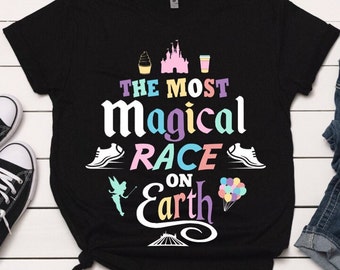 May include: Black t-shirt with a white graphic design that says "The Most Magical Race on Earth". The graphic includes a pink castle, a blue running shoe, a pink ice cream cone, a blue drink, a pink fairy, and a blue hot air balloon.