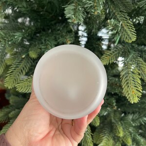 May include: A white frosted glass candle holder with a smooth, rounded surface.