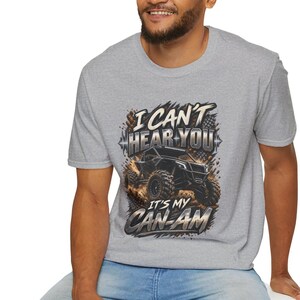Könnte beinhalten: Ein graues, meliertes Kurzarm-T-Shirt mit einem Grafikdruck eines schwarzen Geländewagens, der Staub aufwirbelt. Der Text I CAN'T HEAR YOU IT'S MY CAN-AM ist in einer fetten, metallisch wirkenden Schrift mit einer Schallwelle abgebildet.