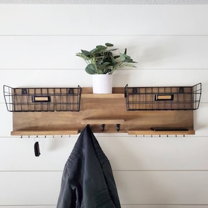 May include: A wooden wall shelf with two black wire baskets, hooks, and a small potted plant. The shelf is mounted on a white wall.