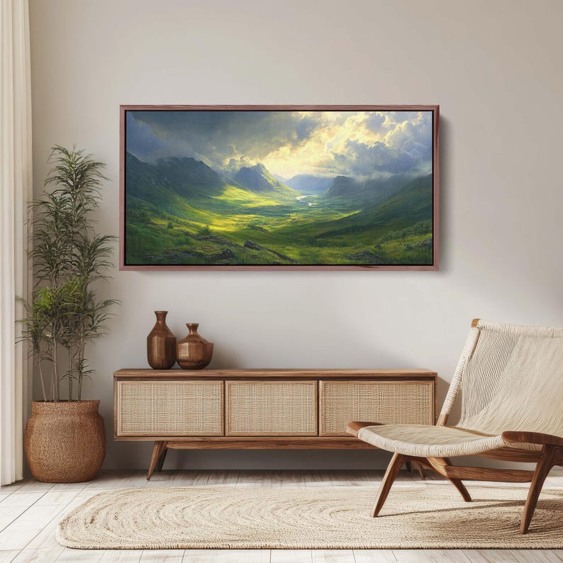 May include: A framed landscape painting depicting a valley with rolling green hills and a river winding through the center. The sky is a mix of blue and gray with white clouds and a bright sun shining through.