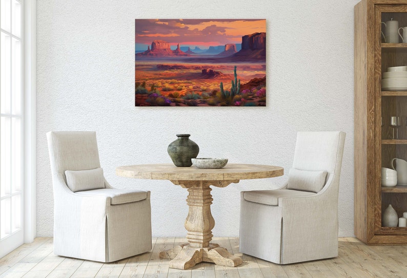 May include: A painting of a desert landscape with red rock formations, a blue sky, and a sunset. The painting is framed and hanging on a white wall above a wooden table with two chairs.