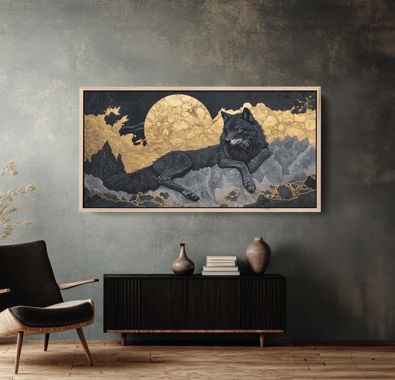 以下が含まれることがあります： 金色の月と雲を背景に、山脈で休む黒いオオカミを描いた額入りのアートワーク。アートワークは、金色のアクセントを持つ暗く、ムードのある美学を持ち、印象的なコントラストを生み出しています。この作品は、暗い家具のある部屋に展示されています。