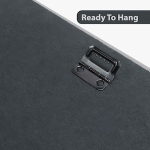 May include: Close-up of a black metal hanging hook attached to the back of a canvas print. The hook is designed to hang the print on a wall. The text "Ready To Hang" is visible in the background.