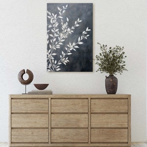 May include: A wooden dresser with six drawers, a white vase with green branches, a brown bowl, and a wooden sculpture on top. A painting of white branches on a dark blue background hangs on the wall above the dresser.