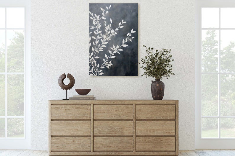 May include: A wooden dresser with six drawers, a white vase with green branches, a brown bowl, and a wooden sculpture on top. A painting of white branches on a dark blue background hangs on the wall above the dresser.