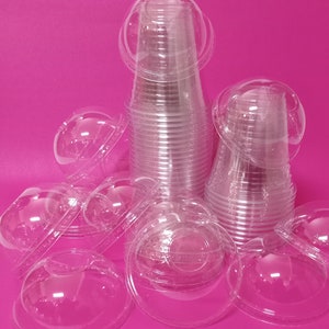 May include: A stack of clear plastic dome lids for cups or bowls. The lids are stacked on a pink surface.