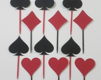 May include: Twelve black and red card suit toppers for cakes or cupcakes. The suits are clubs, diamonds, spades, and hearts.