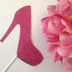 May include: A pink glitter high heel shoe cake topper. The shoe is made of cardboard and has a stick attached to the bottom.