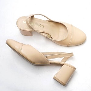 May include: A pair of beige heeled slingback shoes with a block heel. The shoes have a strap that goes around the ankle and a buckle closure. The brand name "My Vision" is printed on the insole.