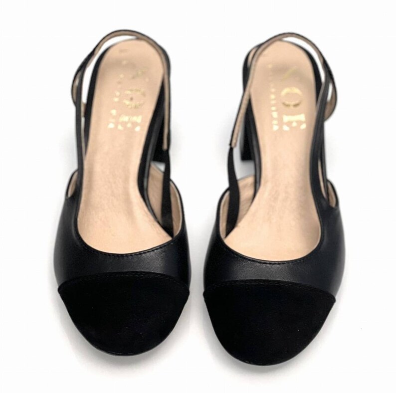 May include: A pair of black leather heeled slingback shoes with a black suede toe cap. The shoes have a slingback strap and a low block heel.