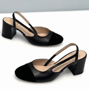 May include: Black leather heeled slingback shoes with a black suede toe cap. The shoes have a block heel and a slingback strap.