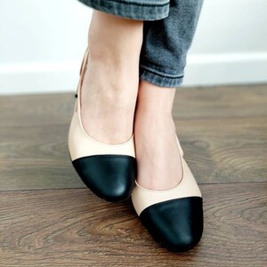 May include: A pair of black and beige two-tone flats with a rounded toe.