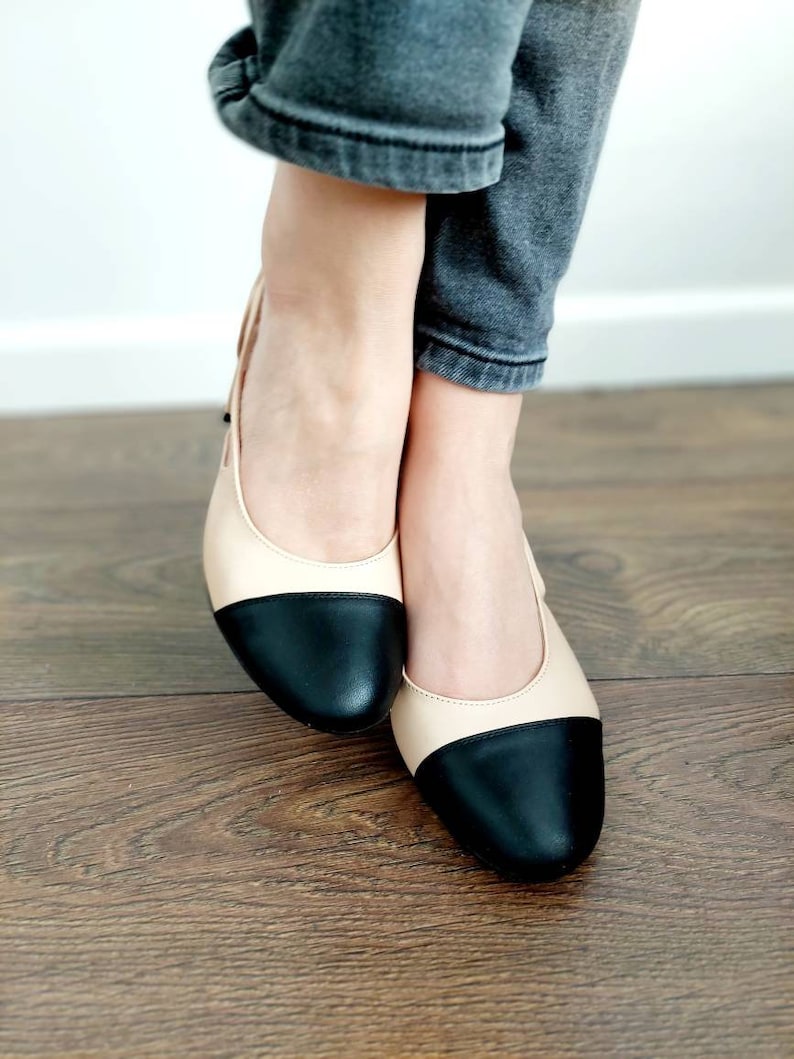 May include: A pair of black and beige two-tone flats with a rounded toe.