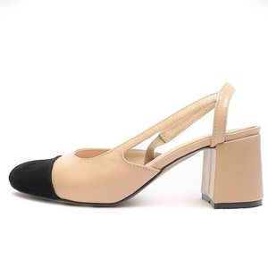 May include: Beige heeled slingback shoes with a black suede toe cap. The shoes have a block heel and an open back.