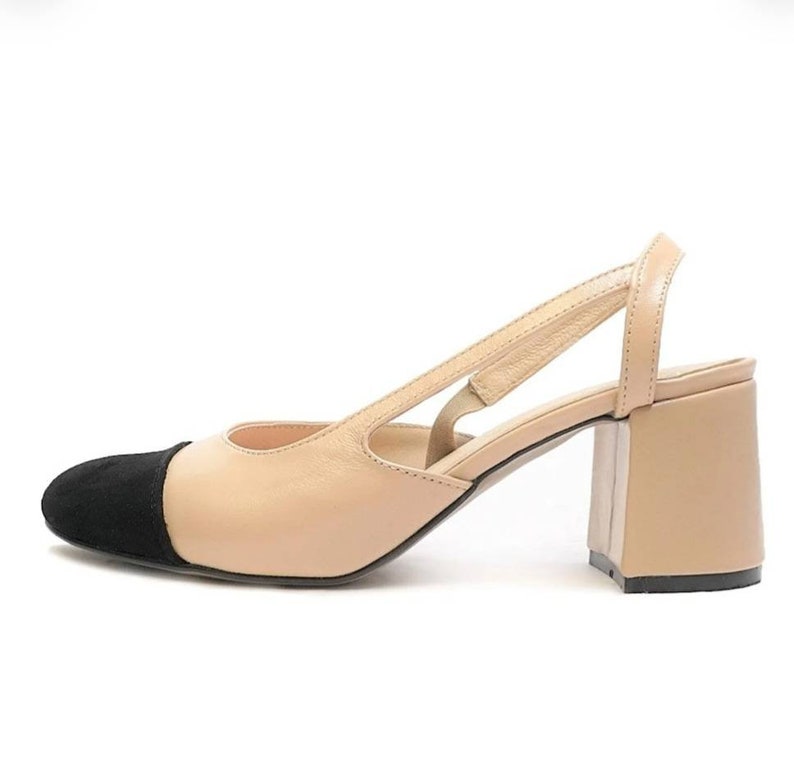 May include: Beige heeled slingback shoes with a black suede toe cap. The shoes have a block heel and an open back.