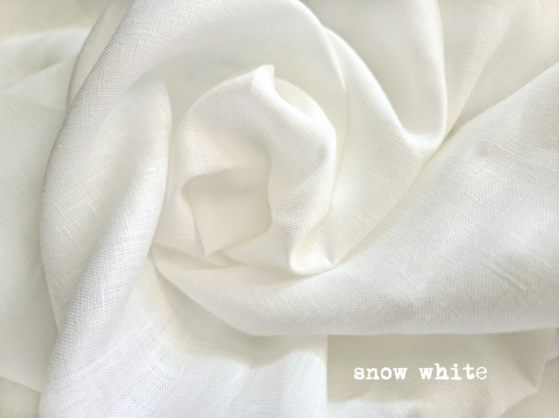 K&ouml;nnte beinhalten: Nahaufnahme eines wei&szlig;en Leinenstoffs, der seine Textur und seinen weichen Fall zeigt. Der Stoff ist glatt und knitterfrei, mit einem dezenten Glanz. Der Text "snow white" ist unten im Bild sichtbar.