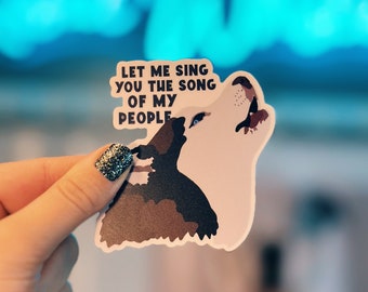 Może przedstawiać: Naklejka z wilkiem wyjącym do księżyca. Naklejka zawiera tekst "Let me sing you the song of my people" w czarnym kolorze.