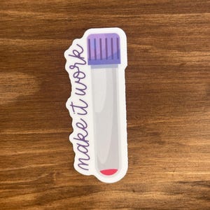 May include: A sticker featuring a cartoon illustration of a test tube with a purple cap and a small amount of red liquid at the bottom. The words "make it work" are written in a cursive font on the left side of the test tube.