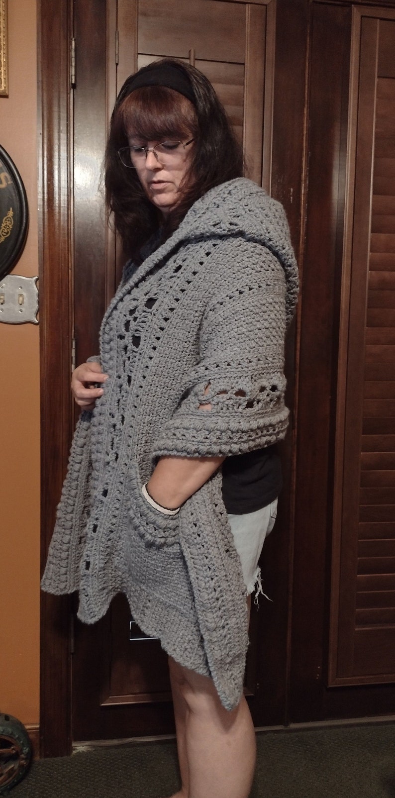 May include: A gray crocheted cardigan with a hood and a pocket. The cardigan is open in the front and has a lacy design.