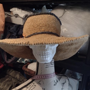 May include: A wide-brimmed straw hat with a dark gray trim around the crown. The hat is sitting on a white mannequin head.