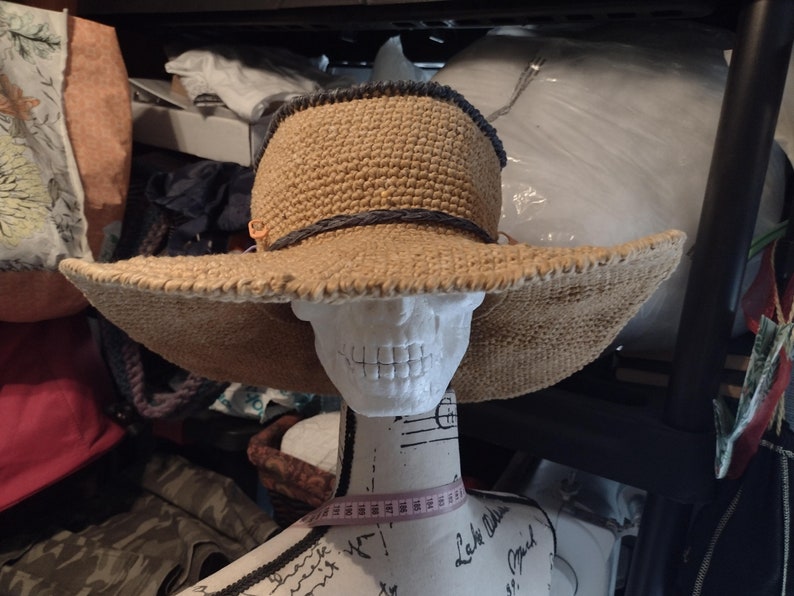 May include: A wide-brimmed straw hat with a dark gray trim around the crown. The hat is sitting on a white mannequin head.