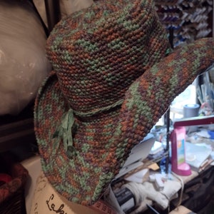 May include: A crocheted hat with a wide brim in shades of green, brown, and purple. The hat has a green ribbon tied around the crown.