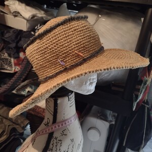 May include: A brown crocheted sun hat with a wide brim and a black trim. The hat is on a white mannequin head.