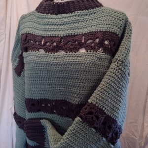 May include: A crocheted sweater with a striped pattern in teal and brown. The sweater has a loose fit and a round neckline.