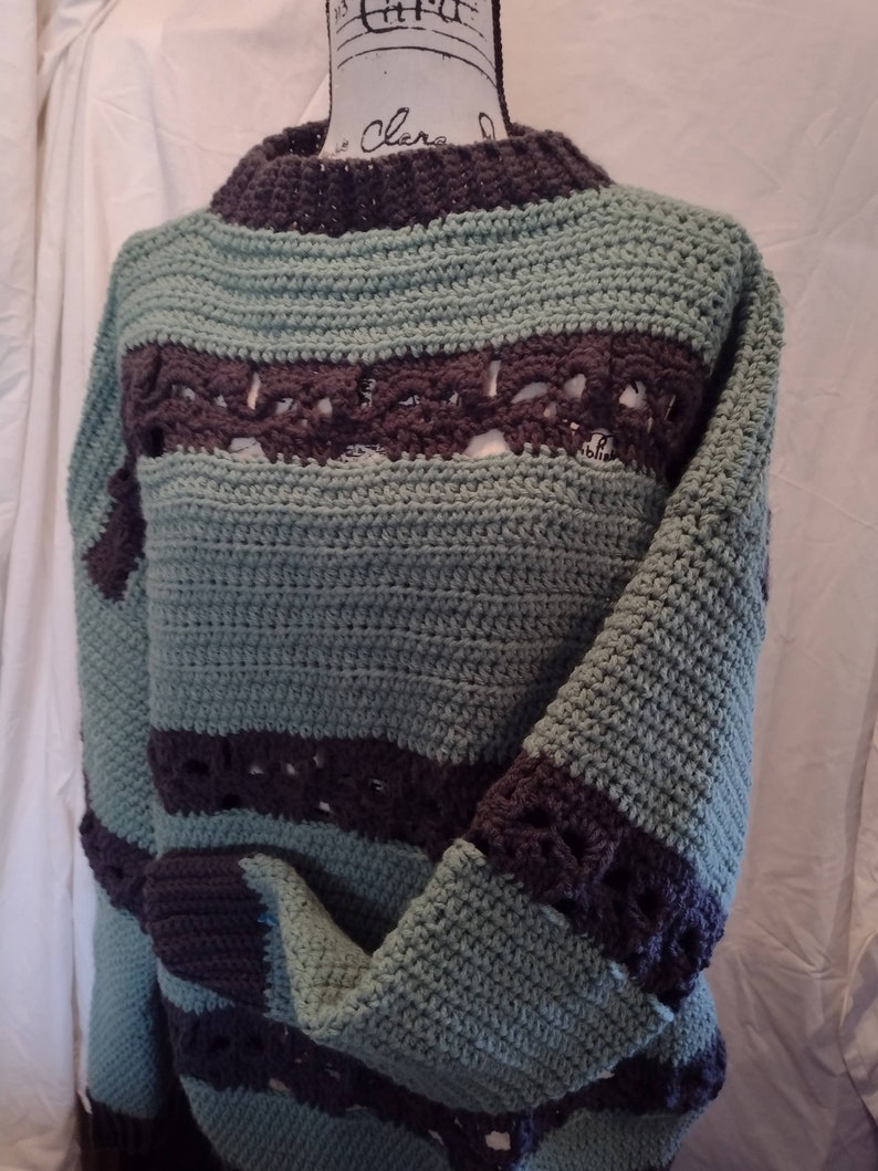 May include: A crocheted sweater with a striped pattern in teal and brown. The sweater has a loose fit and a round neckline.