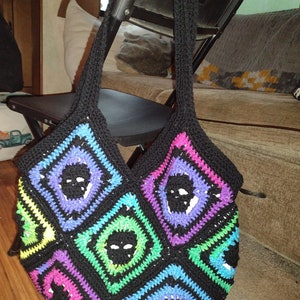May include: A black crocheted tote bag with a skull pattern in various colors, including purple, pink, green, and blue.