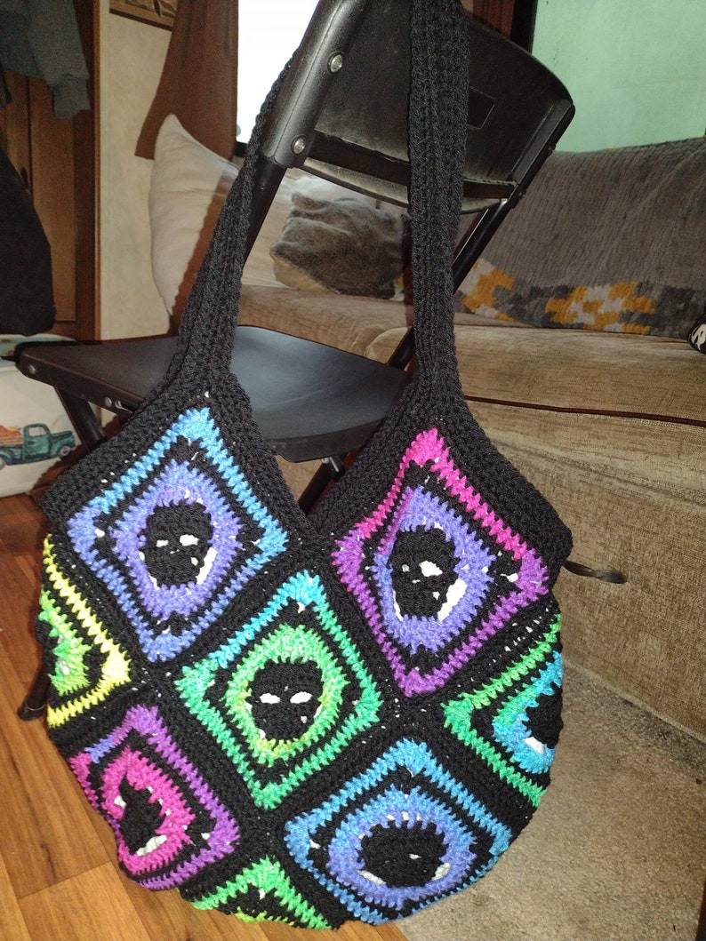 May include: A black crocheted tote bag with a skull pattern in various colors, including purple, pink, green, and blue.