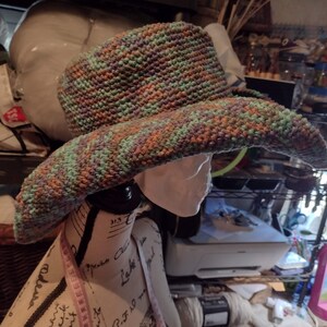May include: A wide-brimmed crocheted hat with a green, brown, and purple color pattern. The hat is on a mannequin head.