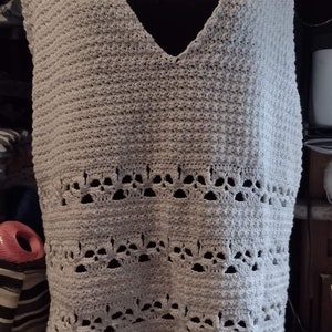May include: A white crocheted sleeveless top with a V-neck and a scalloped hem. The top has a delicate lace pattern.