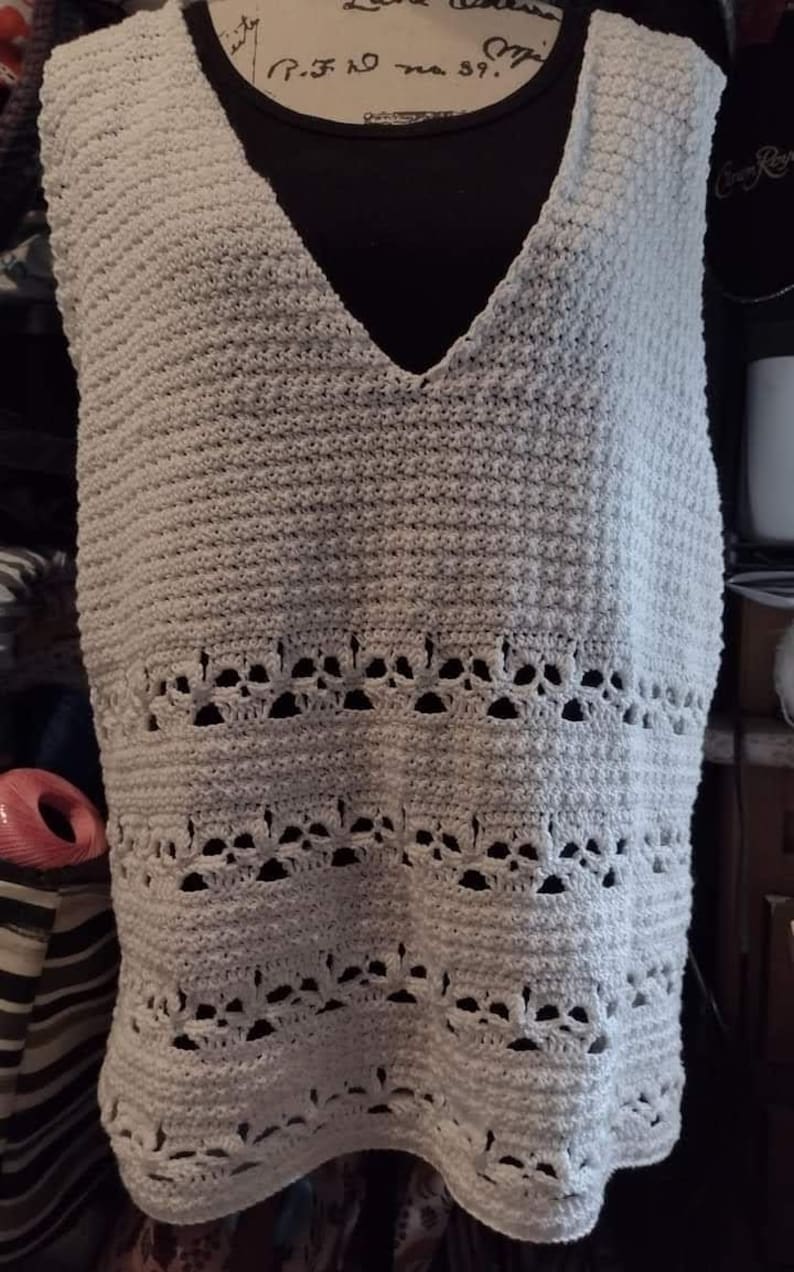 May include: A white crocheted sleeveless top with a V-neck and a scalloped hem. The top has a delicate lace pattern.