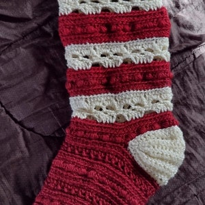 May include: A red and white crocheted Christmas stocking with a white crocheted cuff and a white crocheted toe.
