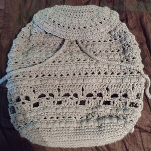 May include: A gray crocheted baby blanket with a hood. The blanket has a delicate openwork pattern and is made with soft yarn.