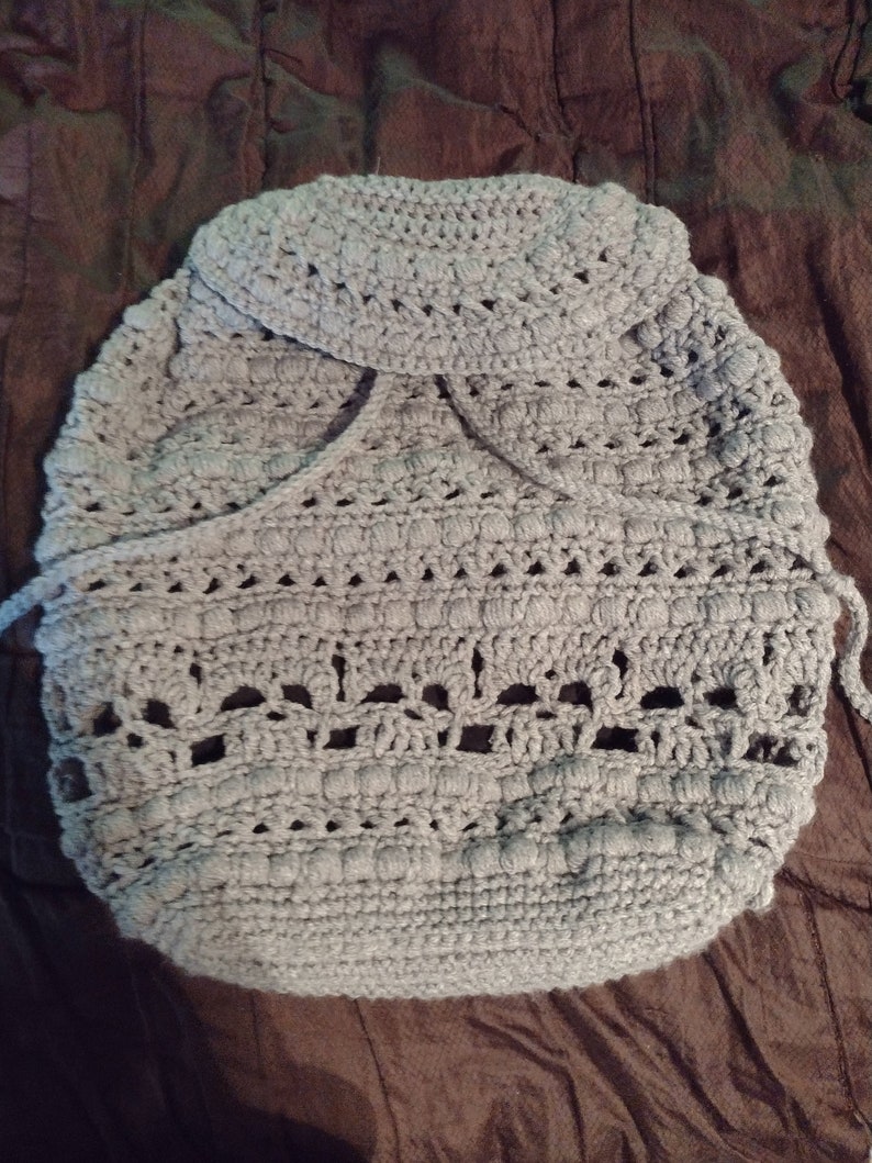 May include: A gray crocheted baby blanket with a hood. The blanket has a delicate openwork pattern and is made with soft yarn.
