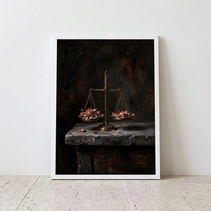 May include: A framed wall art print depicting a brass balance scale resting on a stone surface. The scale pans are filled with dried rose petals and buds in shades of deep red and muted pink, set against a dark, textured, moody background.