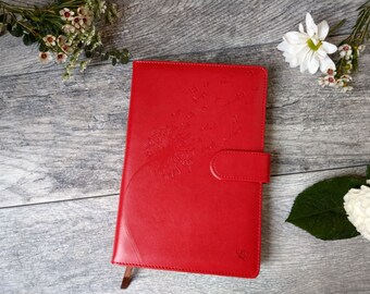 May include: A red leather journal with a dandelion design embossed on the front cover. The journal has a flap closure with a button.