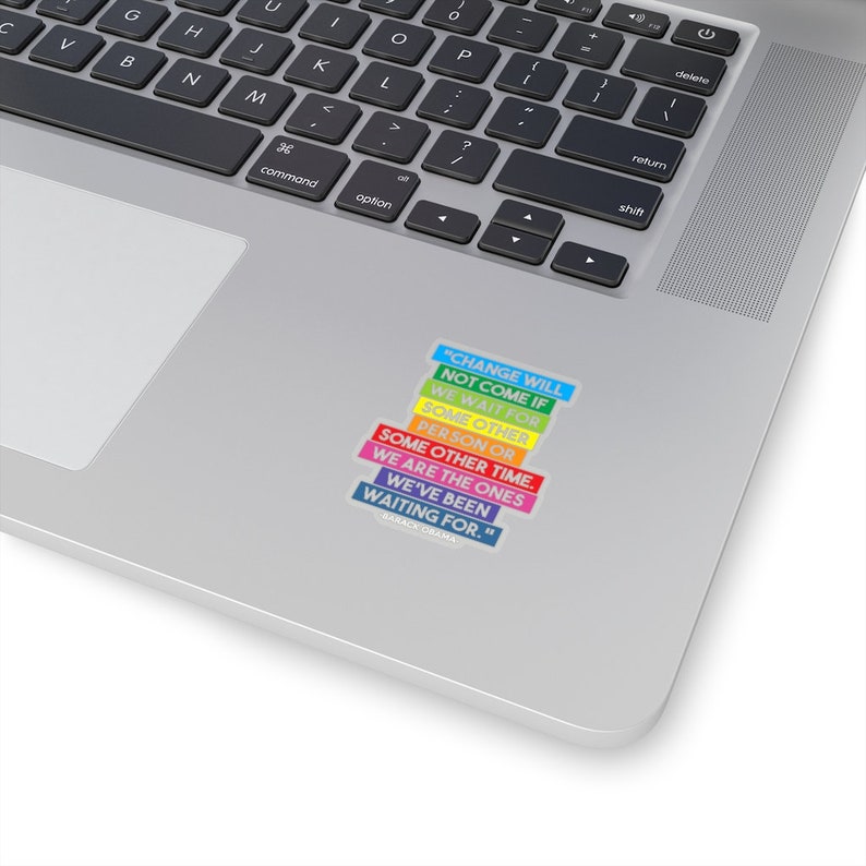 May include: A rainbow-colored sticker with a quote by Barack Obama: "Change will not come if we wait for some other person or some other time. We are the ones we've been waiting for."