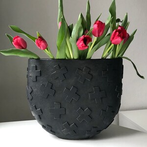 May include: A black ceramic vase with a crosshatch pattern holds a bouquet of pink tulips.
