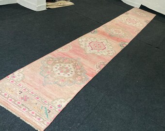 Puede incluir: Una alfombra de pasillo larga y rosa con un patrón floral. La alfombra tiene un fondo rosa claro con un diseño floral rosa oscuro y blanco. La alfombra está colocada sobre una superficie gris oscuro.