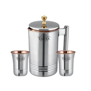 May include: A stainless steel pitcher with a gold-toned lid knob and a side handle, accompanied by two matching stainless steel tumblers. Each piece features a copper-coloured rim and the black printed text TALUKA with decorative flourishes.
