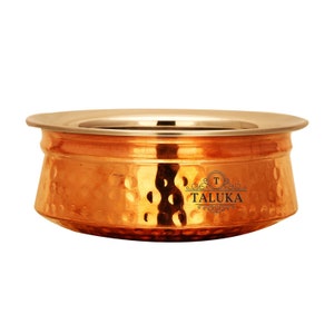 May include: A round, hammered copper serving bowl with a wide, smooth metallic rim. The exterior features a textured, dimpled surface and the black printed text TALUKA with a decorative emblem centered on the side of the vessel.